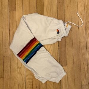 Aviator Nation white sweatpants with rainbow stripe around leg.